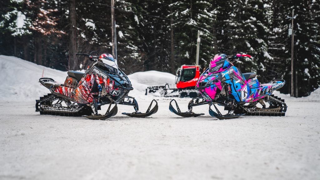 Custom Polaris snowmobiles wrapped by Deviant Ink, featuring John Gibbs’ bold sled setup in a snowy mountain lot.
