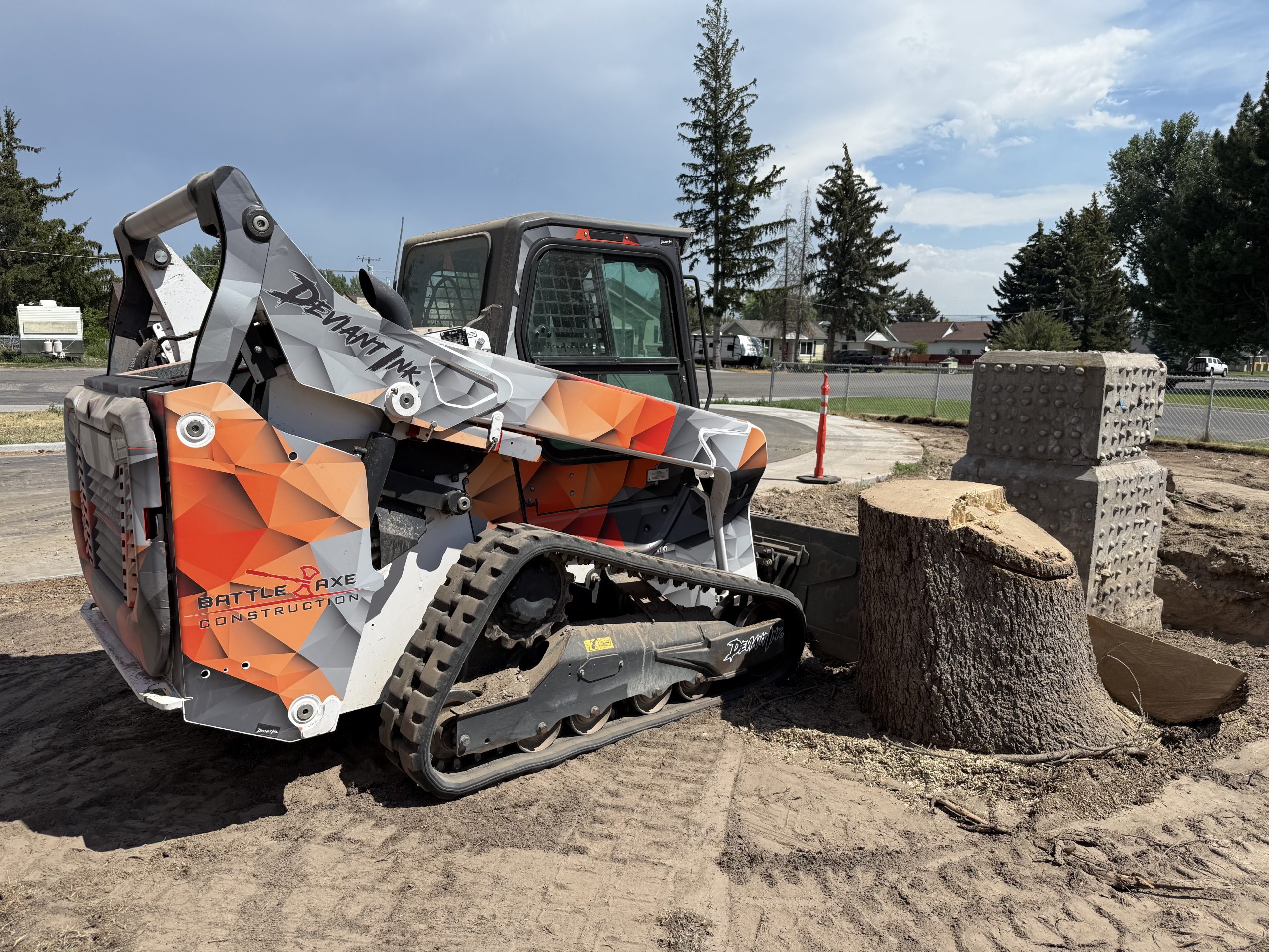 Side-rear view of Bobcat skid steer wrapped in orange and grey Battle Axe Construction design by Deviant Ink