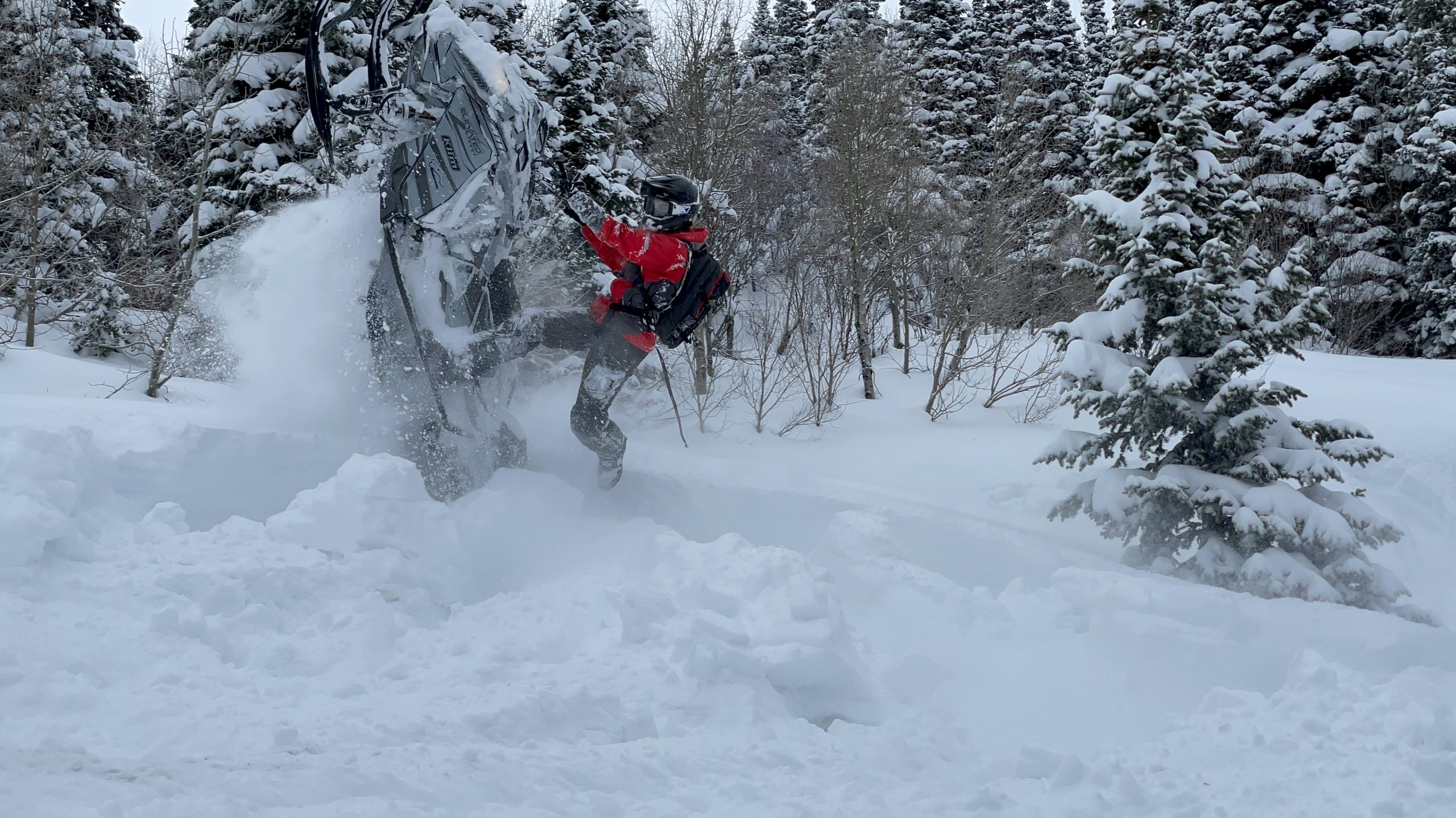 Dylan Boyce performing a vertical snowmobile climb in deep powder on a custom Deviant Ink wrapped sled