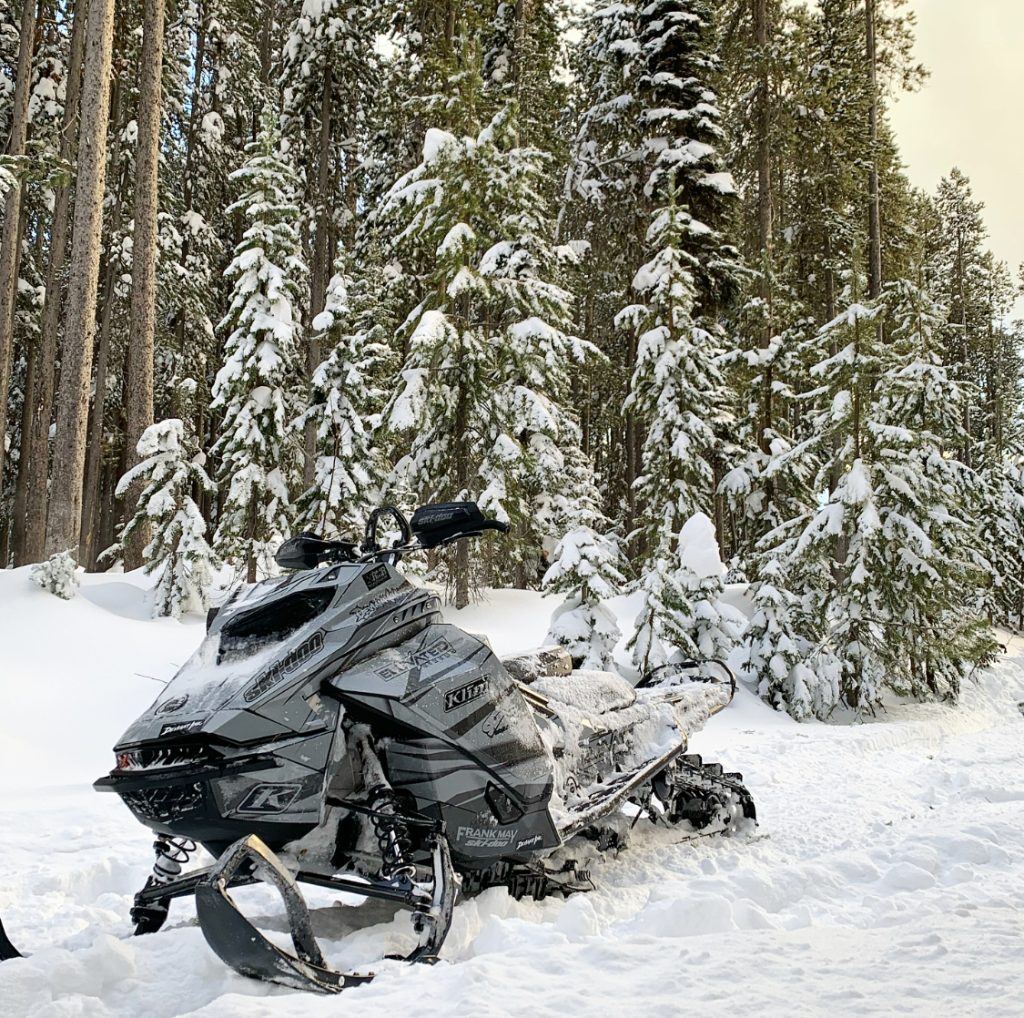 Dylan Boyce’s custom wrapped snowmobile parked in snowy backcountry forest with Deviant Ink graphics